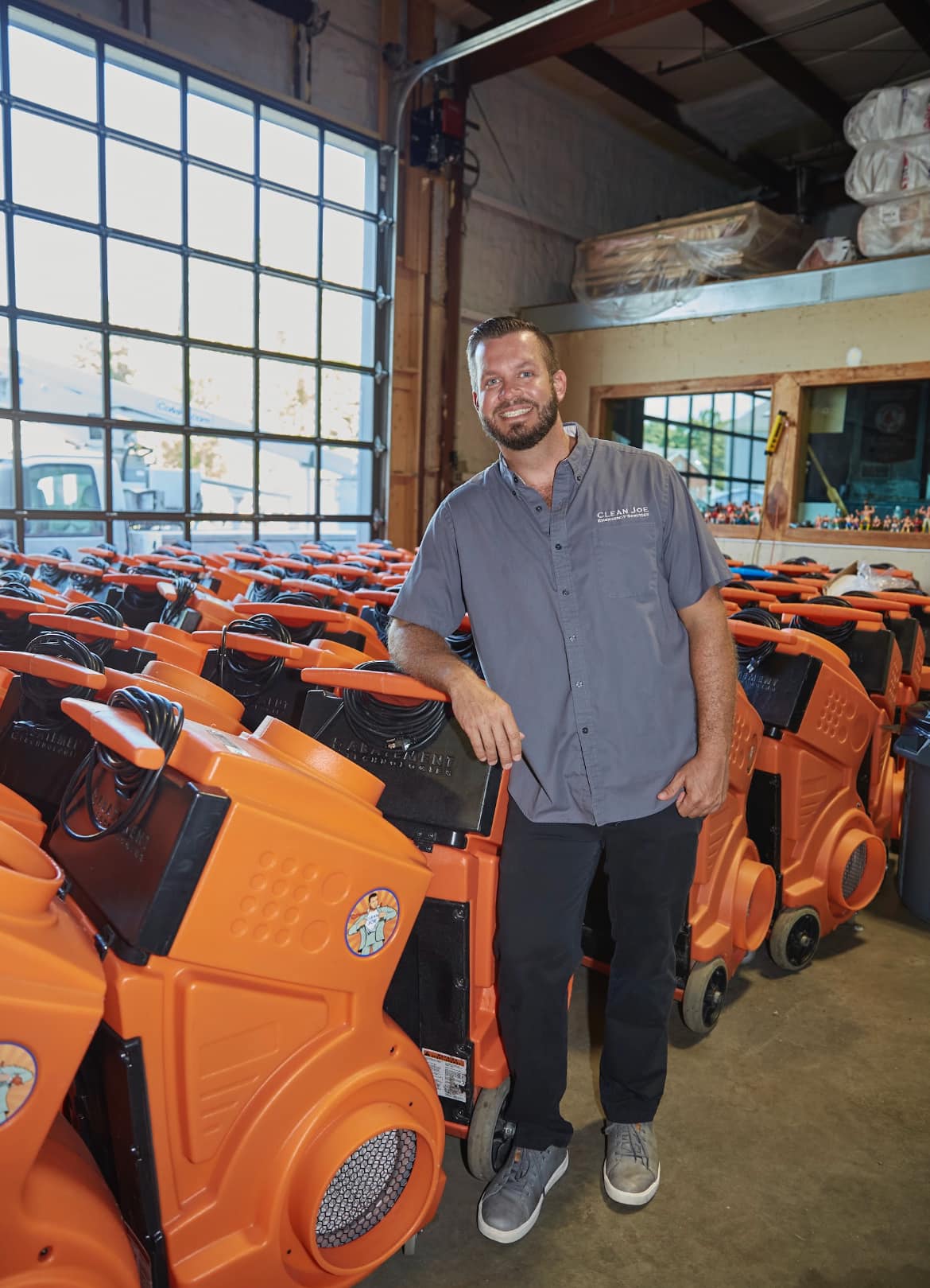 Clean Joe owner standing with rows of orange air movers in the warehouse